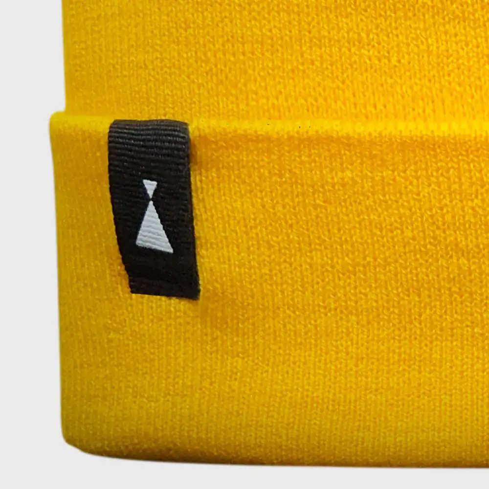 Gorro amarillo de lana con etiqueta negra y símbolo minimalista.