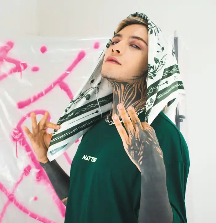 Joven con estilo urbano y tatuajes, usando ropa de Nattivo en un entorno artístico.